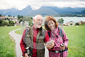 Senior pensioner couple with hiking in nature, using smartphone.