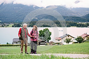 Senior pensioner couple with nordic walking poles hiking in nature, talking.