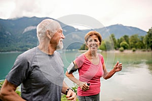 Senior pensioner couple with smartphone running by lake in nature.