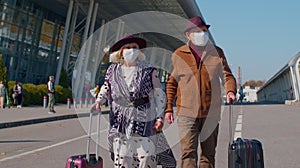 Senior pensioner tourists grandmother grandfather walking from airport with luggage, coronavirus