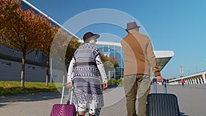 Senior pensioner tourists grandmother grandfather walking to airport hall with luggage on wheels