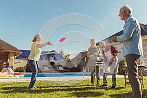 Senior people having fun playing toss and catch at backyard barbecue party