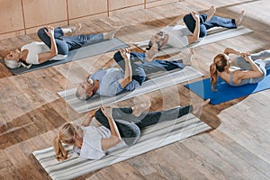 senior people with instructor stretching and exercising on yoga mats