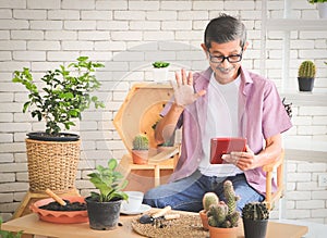 Senior people lifestyle and technology  concept.  Asian elderly man sitting at table with houseplants and gardening tools , making