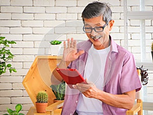 Senior people lifestyle and technology  concept. Close up image of happy Asian elderly man sitting at table with houseplants and