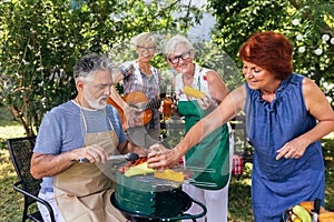 Senior people are making barbeque, drinking beverages, making memories, and laughing