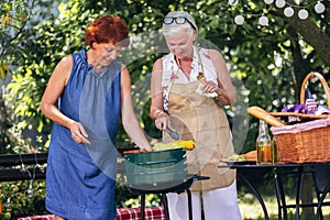 Senior people are making barbeque, drinking beverages, making memories, and laughing