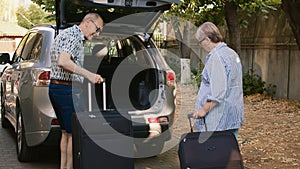 Senior people putting baggage in car trunk