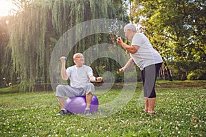 Senior people workout - man and woman doing together fitness exercises on fitness ball in park.