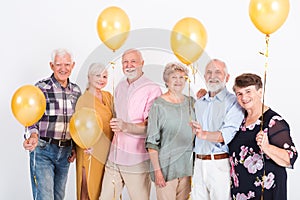 senior people with yellow balloons standing in empty white room