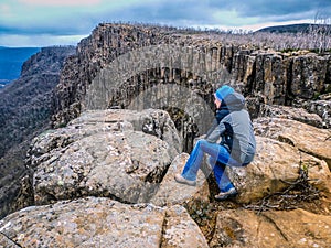 Senior perched on rocks at Devil`s Gullet, Tasmania, looking out into a steep, glacial gorge formed by vertical dolerite cliffs 