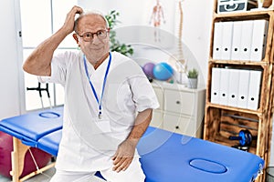 Senior physiotherapy man working at pain recovery clinic confuse and wonder about question