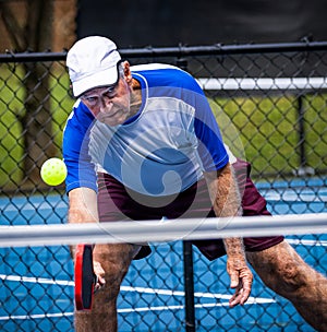 Senior pickleball player digs to return a low dink