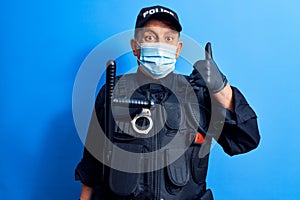 Senior police man wearing surgical mask smiling happy and positive, thumb up doing excellent and approval sign