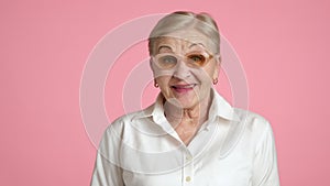 Senior positive woman in glasses standing on pink background nodding approvingly