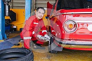 Senior professional Asian male mechanic garage worker happy working tyre wheels replacing car tire maintenance service