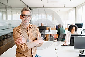 Senior professional is leaning an office desk, confidently overseeing the workspace