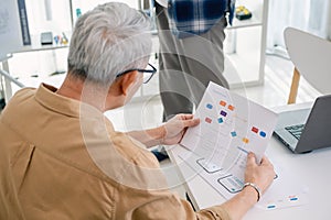 Senior programmer planning software development with flowchart and system process documentation at office