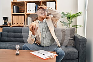 Senior psychiatrist man working at consultation office stressed and frustrated with hand on head, surprised and angry face