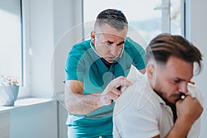 A senior pulmonologist cares for a young male patient, checking lungs, examining his health and discussing treatment