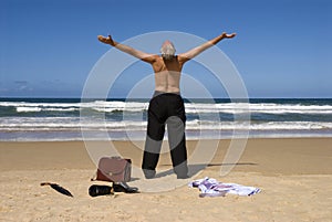 Senior retired business man sunbathing with arms outstretched on tropical caribbean beach, retirement freedom concept