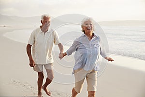 Senior Retired Couple Running Along Beach Hand In Hand Together