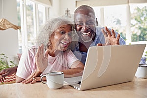 Senior Retired Couple Sitting Around Table At Home Making Video Call On Laptop