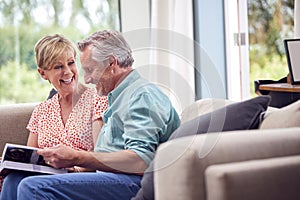 Senior Retired Couple Sitting On Sofa At Home Enjoying Looking Through Family Photo Album