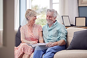 Senior Retired Couple Sitting On Sofa At Home Enjoying Looking Through Family Photo Album