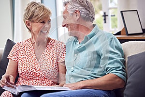 Senior Retired Couple Sitting On Sofa At Home Enjoying Looking Through Family Photo Album