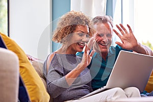 Senior Retired Couple Sitting On Sofa At Home Making Video Call On Laptop