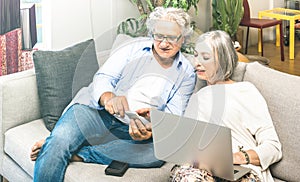 Senior retired couple using laptop computer at home on sofa - Elderly and technology concept with mature people at online shopping