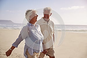 Senior Retired Couple Walking Along Beach Hand In Hand Together