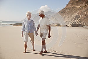 Senior Retired Couple Walking Along Beach Hand In Hand Together