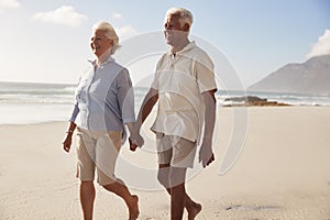 Senior Retired Couple Walking Along Beach Hand In Hand Together