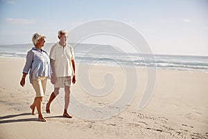 Senior Retired Couple Walking Along Beach Hand In Hand Together