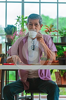 Senior retired man having coffee in a greenhouse garden while surfing on the Internet