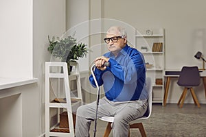 Senior, retired man sitting on a chair at home, leaning on a stick, and thinking