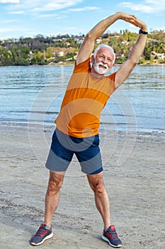 A senior retired man stretching on the beach.