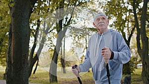 Senior retired old man grandfather practicing Nordic walking use ski trekking poles in summer park