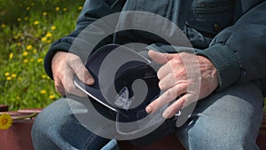 Senior retired old man sitting taking off cap and holding it in hands closeup