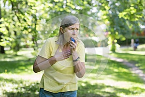 Senior retired woman with asthma breathing in an inhaler in a summer park