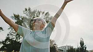 Senior retired woman dancing in the park with outstretched hands low angle shot