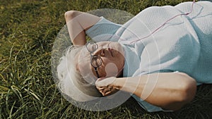 Senior retired woman with headphones lying on the grass and listening to the music