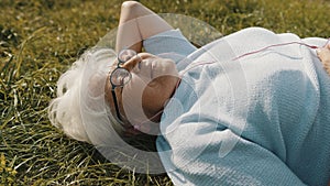 Senior retired woman with headphones lying on the grass and listening to the music