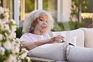 Senior Retired Woman Relaxing On Outdoor Seat At Home Reading Book