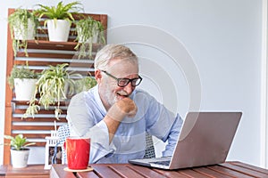 Senior retirement man is enjoy chating with someone using his laptop at home and feeling happy