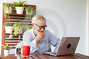 Senior retirement man is enjoy chating with someone using his laptop at home and feeling happy