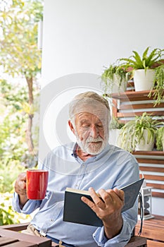 Senior retirement man happy reading book with cup of coffee at home