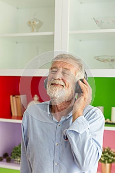 Senior retirement man listen to music using headphone feeling happy in his home